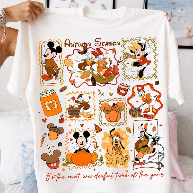 Puede incluir: Una camiseta blanca con un estampado gr&aacute;fico colorido de personajes de Disney en entornos oto&ntilde;ales. El dise&ntilde;o incluye a Mickey, Minnie, Donald, Daisy y Pluto con calabazas, hojas y bellotas. El texto dice Autumn Season y It's the most wonderful time of the year.