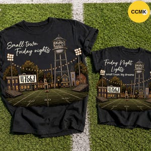 May include: Two black t-shirts featuring a graphic of a football field at night with a water tower, stadium lights, and a scoreboard displaying 47567. The larger shirt reads Small town Friday nights, while the smaller shirt reads Friday Night Lights.