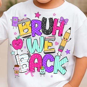 May include: A white t-shirt featuring a colorful graphic with the text BRUH WE BACK. The design includes cartoon school supplies like a notebook, apple, pencil, and coffee cup, decorated with stars, hearts, and bows in pink, yellow, and teal.