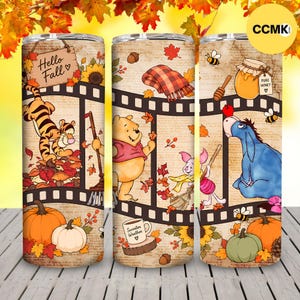 Puede incluir: Tres vasos cilíndricos con un diseño de tira de película vintage con personajes de Winnie the Pooh, hojas de otoño, calabazas, un tarro de miel y una manta a cuadros. El texto incluye Hello Fall y Sweater Weather sobre fondo beige.