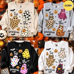 May include: Four crewneck sweatshirts in beige, gray, black, and white, each featuring a graphic print of three ghosts holding pumpkins, small bats, and the text 'tis the season' in a cursive font, with various patterns on the ghosts.