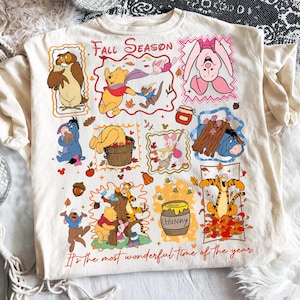 Puede incluir: Una camiseta de color crema con un collage de personajes de Winnie the Pooh, incluyendo a Piglet, Eeyore, Tigger y Owl. El gr&aacute;fico incluye el texto "Fall Season" y "It's the most wonderful time of the year" con varias ilustraciones oto&ntilde;ales como hojas, bellotas y un tarro de miel.
