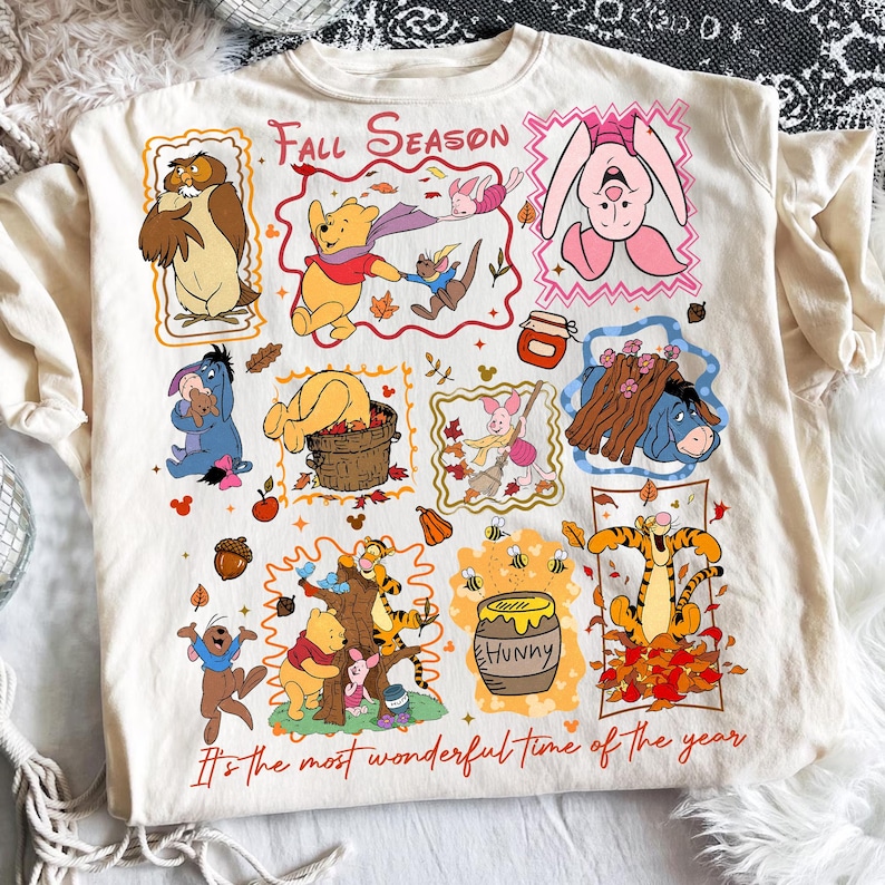 Puede incluir: Una camiseta de color crema con un collage de personajes de Winnie the Pooh, incluyendo a Piglet, Eeyore, Tigger y Owl. El gr&aacute;fico incluye el texto "Fall Season" y "It's the most wonderful time of the year" con varias ilustraciones oto&ntilde;ales como hojas, bellotas y un tarro de miel.