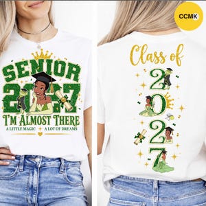 May include: A white t-shirt featuring a green glitter graphic on the front that reads SENIOR 2027 I'M ALMOST THERE A LITTLE MAGIC A LOT OF DREAMS with a cartoon character in a graduation cap. The back displays Class of 2027 with glittery numbers.
