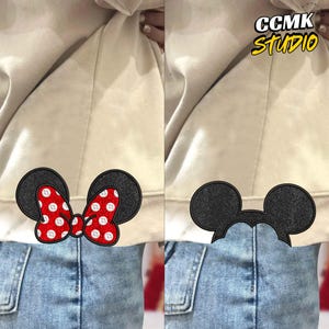 May include: Two decorative patches featuring cartoon mouse ears. One patch has black ears and a red bow with white polka dots. The other patch has black ears. The patches are on a light-coloured jacket and blue jeans. The text "CCMK STUDIO" is in the upper right corner.