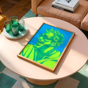 Könnte beinhalten: Ein gerahmter Pop-Art-Druck mit einer Person mit grünen Haaren und Sonnenbrille vor blauem Hintergrund. Auf einem hellrosa runden Couchtisch stehen vier grüne Trinkgläser auf einem weißen Tablett.