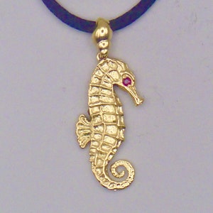 May include: A gold seahorse pendant with a red gemstone eye, hanging from a black cord.