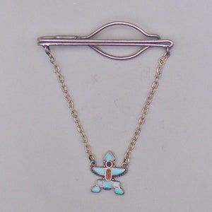May include: A silver tie clip with a chain and a turquoise and red geometric pendant.