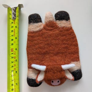 May include: A handmade felted Highland cow, with a brown body, black hooves, and white horns. The cow is approximately 10 cm long. The felted animal is a unique decorative item.
