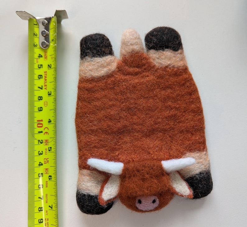 May include: A handmade felted Highland cow, with a brown body, black hooves, and white horns. The cow is approximately 10 cm long. The felted animal is a unique decorative item.