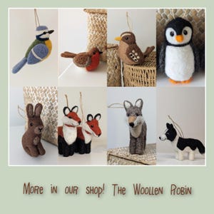 May include: A selection of felt animal decorations, featuring a blue tit, robin, penguin, rabbit, fox, wolf, and a black and white dog. Each ornament is crafted with detailed colours and textures, and includes a hanging string. The text "More in our shop! The Woollen Robin" is displayed at the bottom.