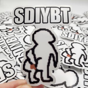 May include: White sticker with black outline featuring a pixelated figure holding a bag, with the text "SDIYBT" above. The sticker has a white background and is surrounded by other similar stickers.