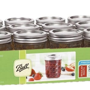 Op de afbeelding: Een dozijn 240ml Ball Quilted Crystal Jelly Jars met zilveren deksels, in een groen en bruin kartonnen doos. De doos toont een pot gevuld met gelei en fruit. De potten zijn vriezerbestendig en gemaakt in de VS.