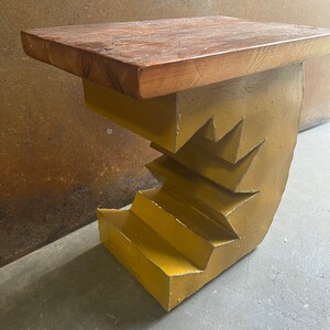 K&ouml;nnte beinhalten: Ein gelber Metall-Beistelltisch mit einer Holzplatte. Der Metallsockel ist in Form einer Treppe gestaltet.