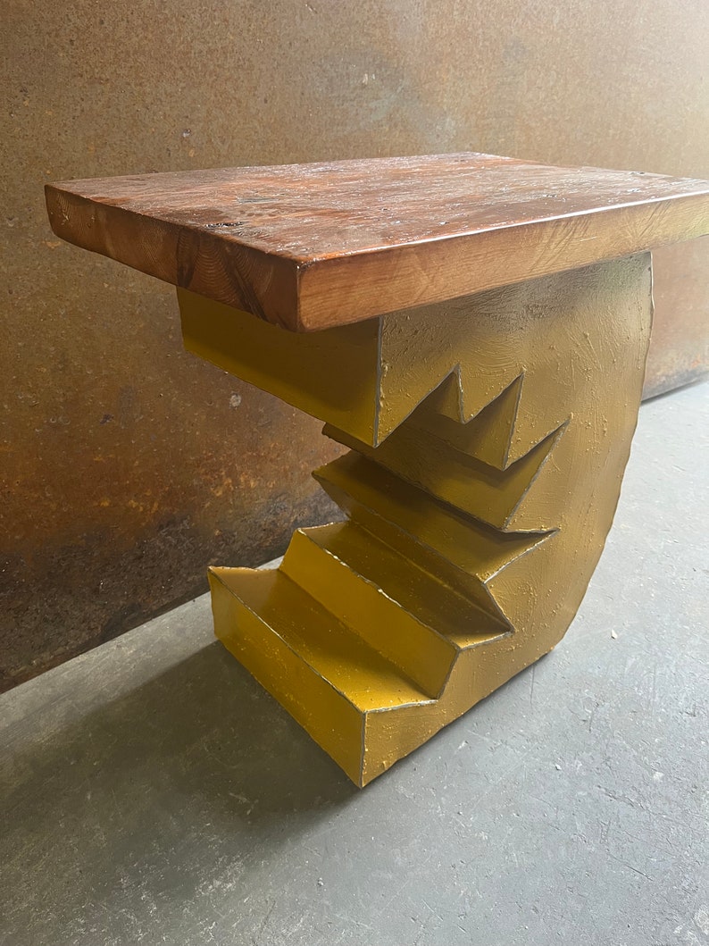 K&ouml;nnte beinhalten: Ein gelber Metall-Beistelltisch mit einer Holzplatte. Der Metallsockel ist in Form einer Treppe gestaltet.
