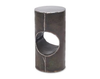 May include: A dark gray metal stool with a circular cutout in the middle. The stool has a rough, industrial look.