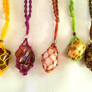 May include: Five colorful macrame necklaces with different colored stones in a net-like pouch. The necklaces are made with different colored cords and have a silver bead at the top.