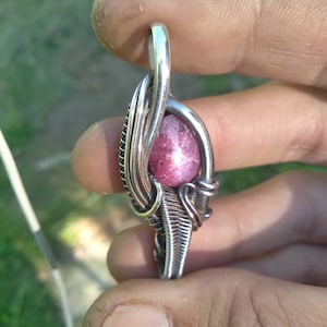 以下が含まれることがあります： ピンクのスターバーストジェムストーンを特徴とするシルバーワイヤーラップペンダント