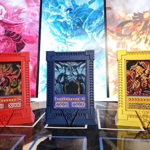 Könnte beinhalten: Drei farbenfrohe Yu-Gi-Oh!-Karten-Displays. Das rote Display zeigt eine Drachenillustration, das blaue ein Monster und das gelbe einen weiteren Drachen. Jedes Display hat ein einzigartiges Design und Kartendetails.