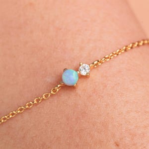 May include: A delicate gold chain bracelet with a small opal and a clear gemstone.