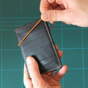 Trifold wallet with orange elastic band and coin pocket made from recycled inner bike tubes.