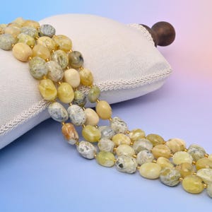 May include: A strand of yellow, green, and white oval-shaped gemstone beads. The beads have a natural, rough texture and are strung on a gold thread.