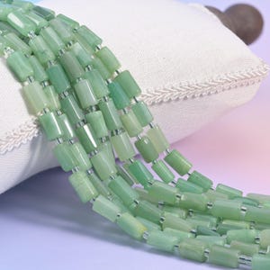 May include: A strand of cylindrical beads in varying shades of light and mint green. The beads have a smooth, polished finish and are strung together on a thin, clear filament, creating a continuous, flexible line of uniform, tube-shaped pieces.
