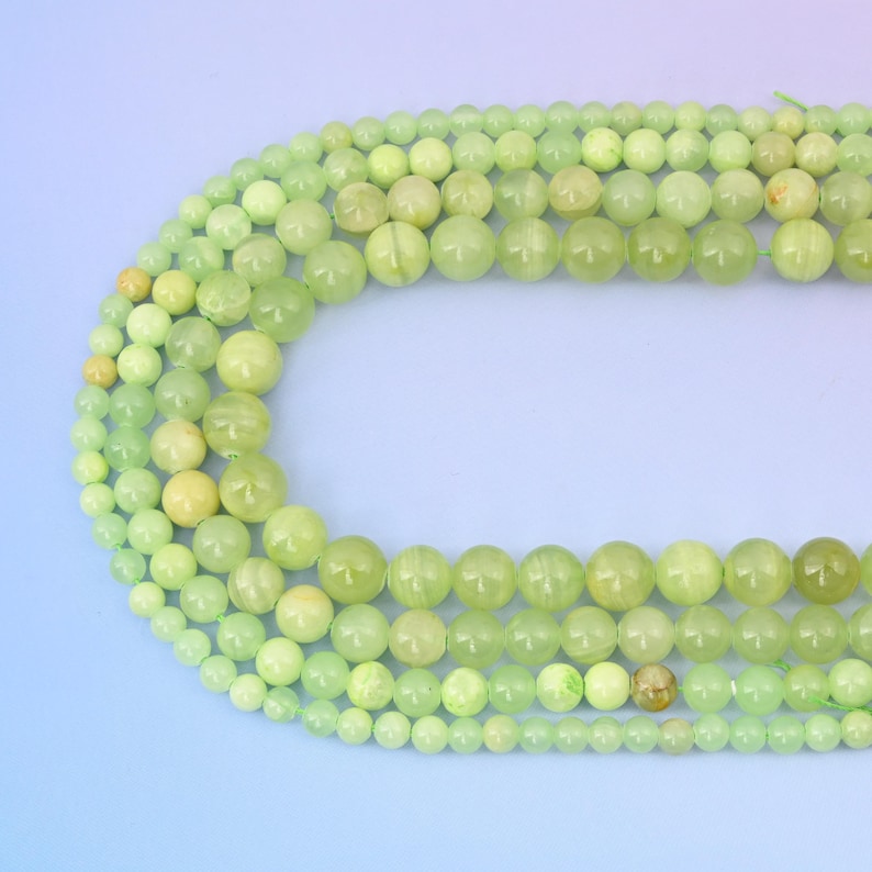 May include: A strand of light green jade beads, with varying sizes, arranged in a circular pattern on a light blue background.