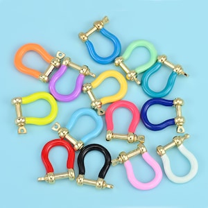 May include: A collection of colorful, U-shaped metal shackle clasps in various colors, including orange, purple, yellow, blue, red, pink, green, and black. Each clasp has a gold-colored metal pin and base, set against a light blue background.