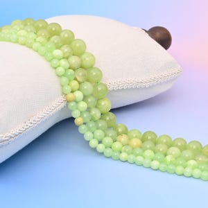 May include: A strand of light green and yellow gemstone beads. The beads are round and smooth, and they are strung on a clear thread. The beads are arranged in a loose, flowing pattern.