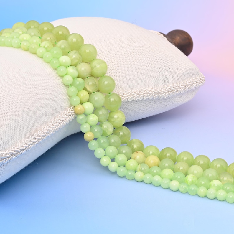 May include: A strand of light green and yellow gemstone beads. The beads are round and smooth, and they are strung on a clear thread. The beads are arranged in a loose, flowing pattern.