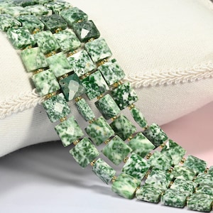 May include: Three strands of square-cut, faceted green and white mottled gemstone beads arranged in parallel rows. Each bead is separated by a small, round, metallic gold-colored spacer bead, creating a uniform and structured appearance.