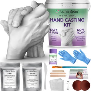 May include: A hand casting kit with two pairs of hands in a mold, a bucket of casting powder, a bottle of sealant, two pairs of blue gloves, a paintbrush, a wooden stick, two white cloths, a safety pin, two brown circles, and two bags of casting powder and stone. The bucket has the text "Luna Bean The Original Hand Casting Kit Easy & Fun Couples Families Friends Non-Toxic Hypoallergenic Quick Setting Skin Safe" on it.