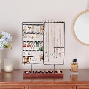 May include: Black metal jewelry stand with a wooden base. The stand has multiple hooks for necklaces and a grid for earrings. There are also slots for rings.