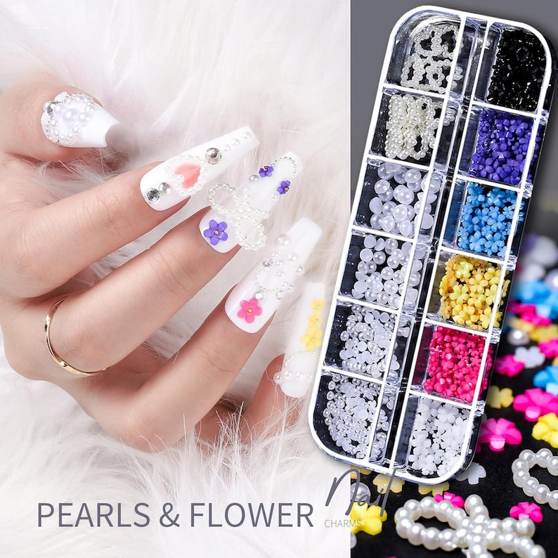 Op de afbeelding: Witte acrylnagels versierd met parels en bloemvormige bedels. Een doorzichtige plastic organizer bevat nail art versieringen in verschillende maten en kleuren. De tekst "PEARLS & FLOWER" staat onderaan de afbeelding.