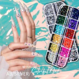Op de afbeelding: Afbeelding van twee handen met lange, versierde nagels. De nagels zijn versierd met zilveren glitter en strass-steentjes. Twee bakjes met kleurrijke nail art strass-steentjes staan op de achtergrond. De tekst "AB/SILVER/ Colorful Nail CRYSTAL" staat onderaan.