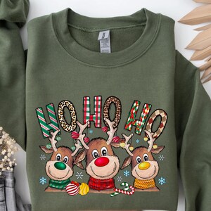 May include: Military green sweatshirt with a festive design. The graphic features three reindeer with colorful scarves and the text "HO HO HO" in a mix of patterns. Christmas-themed apparel.