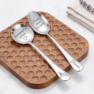 Può includere: Due cucchiai in metallo argentato con testo e grafiche incise. Un cucchiaio presenta la scritta "Soulmate's spoon" con un'icona a forma di cuore. L'altro mostra "Happy 20th Birthday" nella coppa e "Diana" con un'icona di uccellino sul manico.