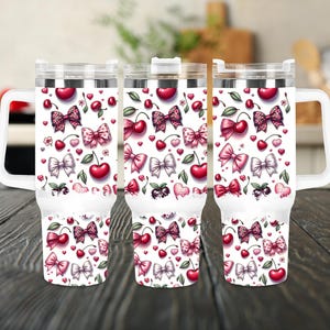 May include: Three white stainless steel travel mugs with a handle. The mugs are decorated with a pattern of pink bows, red cherries, and green leaves on a white background.