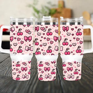 Pode incluir: Três copos de aço inoxidável com desenhos de cerejas e laços rosa e branco. Os copos têm uma alça e uma tampa.