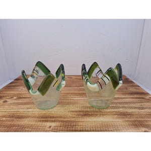 May include: Two clear glass bowls with a unique design. The rims are shaped like a crown, with green and white accents. The bowls are sitting on a wooden surface.