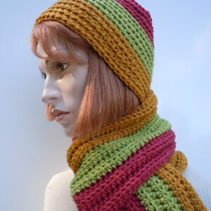 Op de afbeelding: Een gebreide set van muts en sjaal in tinten mosterdgeel, groen en bordeauxrood. De muts is een slouchy beanie-stijl en de sjaal is lang en breed.
