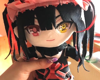 以下が含まれることがあります： 黒髪、赤い目、黄色の目をした女性アニメキャラクターのぬいぐるみ。黒と赤のドレスを着て、ピンクと赤のリボンをつけています。おもちゃは手で持たれています。