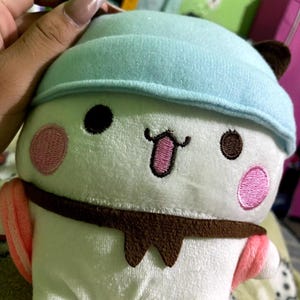 Puede incluir: Juguete de peluche blanco con un sombrero azul, ojos marrones, mejillas rosadas y un bigote marr&oacute;n. El juguete lleva una bufanda marr&oacute;n y tiene detalles rosas y blancos.