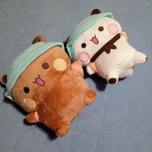 Puede incluir: Dos peluches, un oso marr&oacute;n con un gorro azul y blanco y un oso blanco con un gorro azul y blanco. Ambos osos tienen ojos negros y mejillas rosadas.