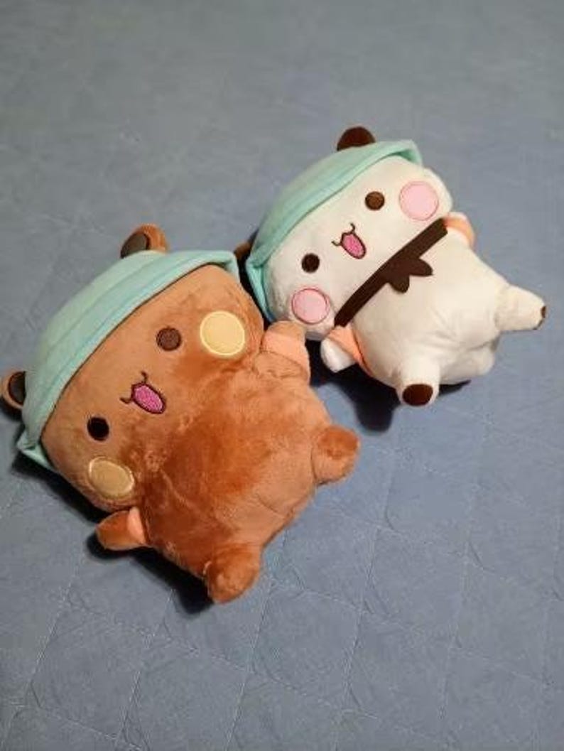 Puede incluir: Dos peluches, un oso marr&oacute;n con un gorro azul y blanco y un oso blanco con un gorro azul y blanco. Ambos osos tienen ojos negros y mejillas rosadas.