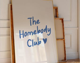 May include: A white framed canvas print with the text "The Homebody Club" in blue handwriting with a blue heart symbol.