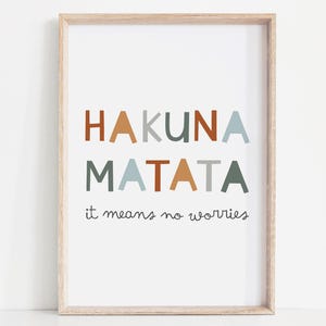 Può includere: Una stampa incorniciata con le parole "HAKUNA MATATA" in lettere a blocchi colorate. Sotto, la frase "it means no worries" è scritta in corsivo. La cornice è di colore legno chiaro.