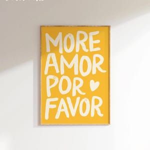 Peut inclure: Impression jaune encadr&eacute;e avec les mots "MORE AMOR POR FAVOR" en blanc, avec un symbole de c&oelig;ur. Les mots "T&Eacute;L&Eacute;CHARGEMENT NUM&Eacute;RIQUE" sont dans le coin sup&eacute;rieur gauche. L'impression est affich&eacute;e sur un mur blanc.