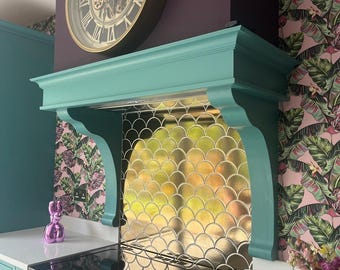 May include: A teal green kitchen with a gold mosaic backsplash behind a black electric stovetop. The kitchen has a dark purple wall with a large gold clock with Roman numerals and gears. The opposite wall has pink and green tropical leaf wallpaper.